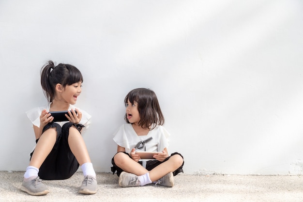 Hermanas disfrutan usando teléfonos inteligentes sobre fondo blanco, el concepto de tecnología de la comunicación