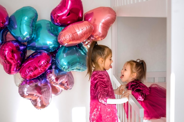 Las hermanas divertidas están sentadas junto a la cama burlándose y mostrando su lengua