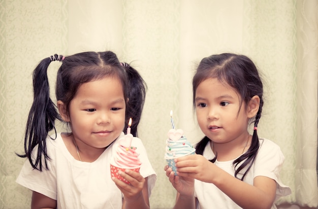 Hermanas se divierten soplando cupcake de cumpleaños juntos, tono de color Vintage