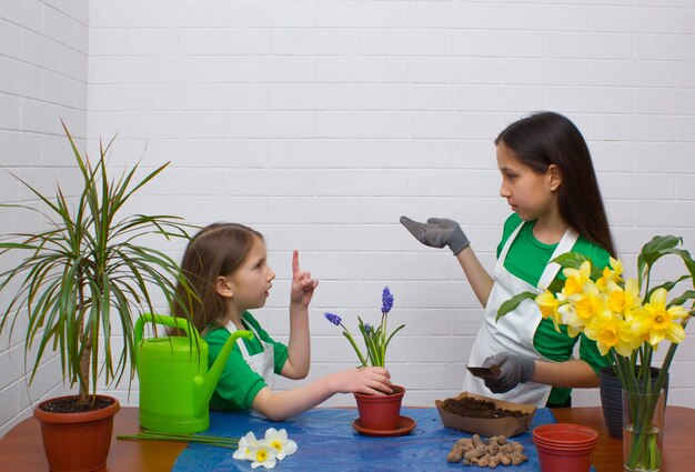 Hermanas de dos niñas trasplantan flores, la niña más joven apunta hacia arriba con su dedo índice para tener una idea
