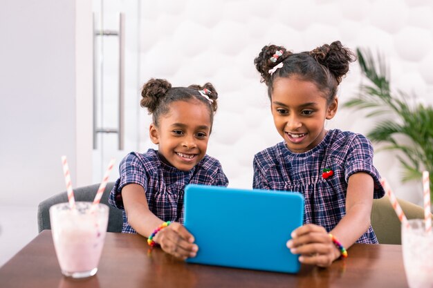 Hermanas emocionadas. Hermanas sonrientes de ojos oscuros que se sienten emocionadas mientras miran dibujos animados en tableta azul