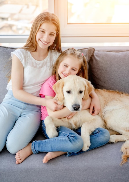 Hermanas felices abrazando a un perro lindo sentado en un sofá en casa