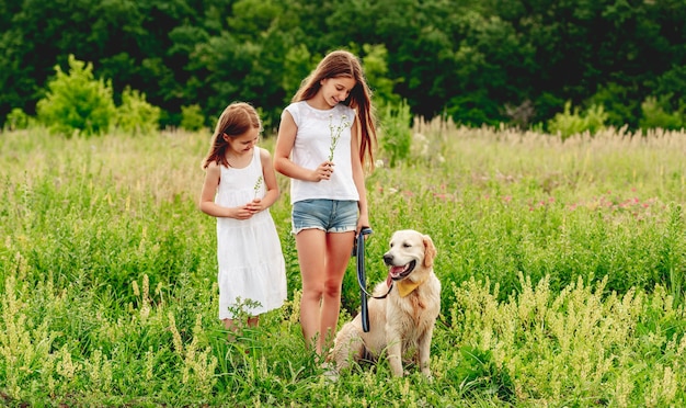 Hermanas felices con lindo perro en pradera de verano floreciente