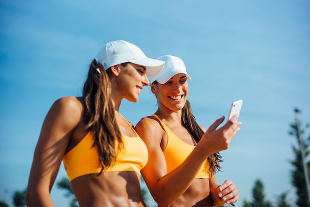 Hermanas gemelas con gorra usando teléfono celular móvil