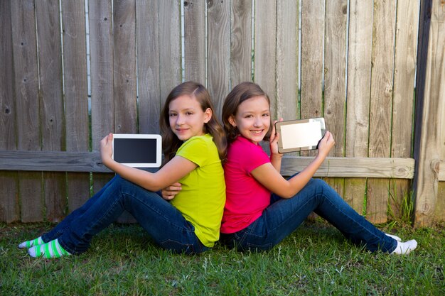 Hermanas gemelas hermanas jugando tablet pc sentadas en el jardín del patio