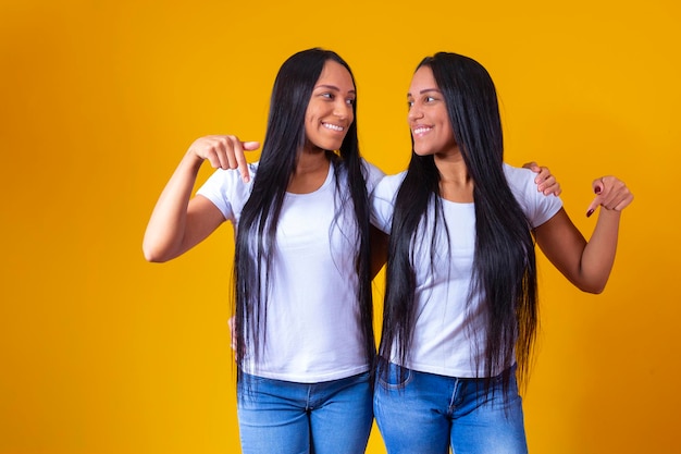 Hermanas gemelas idénticas apuntando hacia abajo con camiseta blanca y espacio de copia