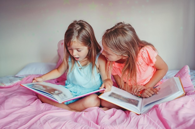 Hermanas leyendo libros mientras están sentadas en la cama en casa