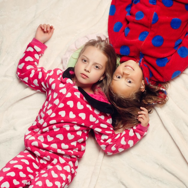 Foto hermanas de niña en pijama se encuentran en la cama, vista superior