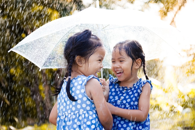 Hermanas con paraguas divirtiéndose jugando bajo la lluvia