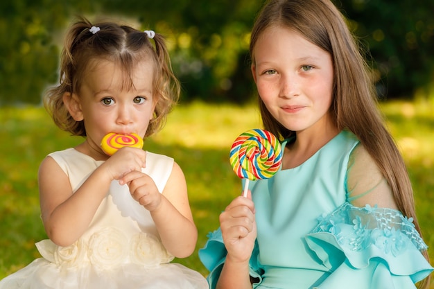 Hermanas con piruletas dulces en la naturaleza en el verano en el parque