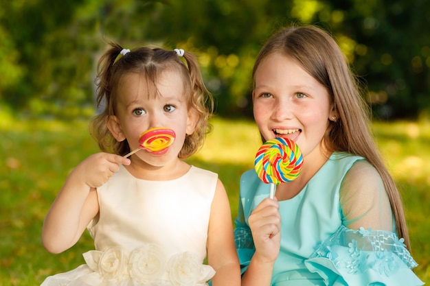 Hermanas con piruletas dulces en la naturaleza en el verano en el parque