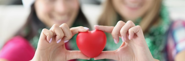 Hermanas sosteniendo un corazón rojo de plástico en las manos y sonriendo