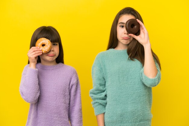 Hermanitas aisladas sobre fondo amarillo con rosquillas en los ojos con expresión triste