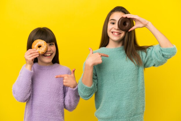 Hermanitas aisladas sobre fondo amarillo sosteniendo una rosquilla y feliz