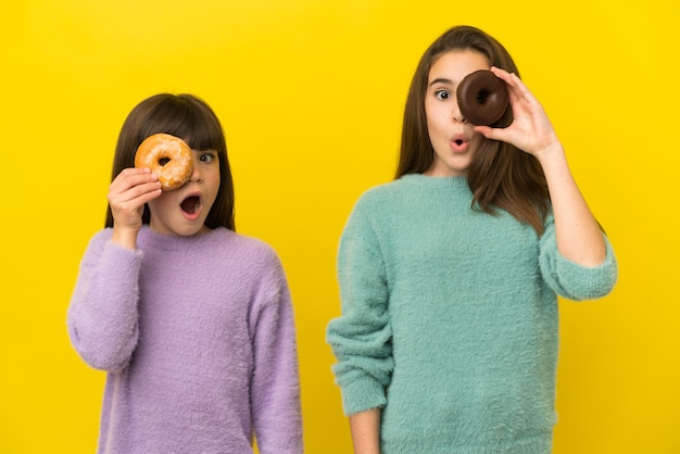 Hermanitas aisladas sobre fondo amarillo sosteniendo una rosquilla en un ojo