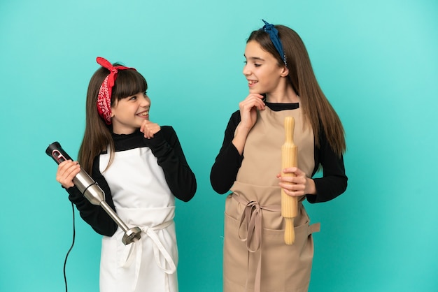 Hermanitas cocinar en casa aislado sobre fondo azul mirando el uno al otro