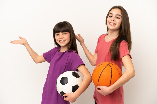 Hermanitas jugando al fútbol y baloncesto aislado sobre fondo blanco extendiendo las manos hacia el lado para invitar a venir