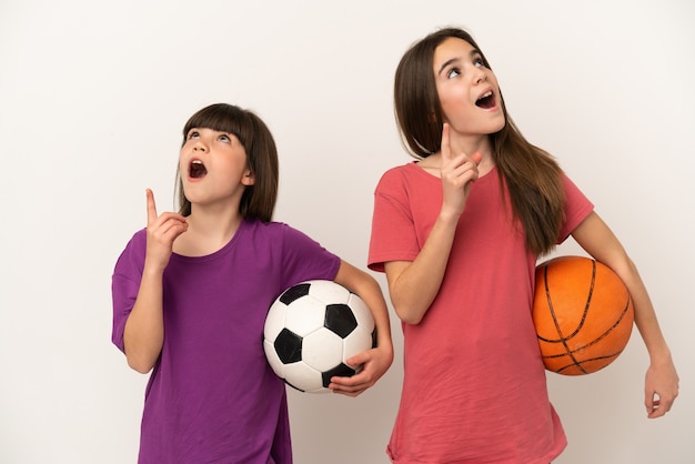 Hermanitas jugando al fútbol y baloncesto aislado sobre fondo blanco pensando en una idea apuntando con el dedo hacia arriba
