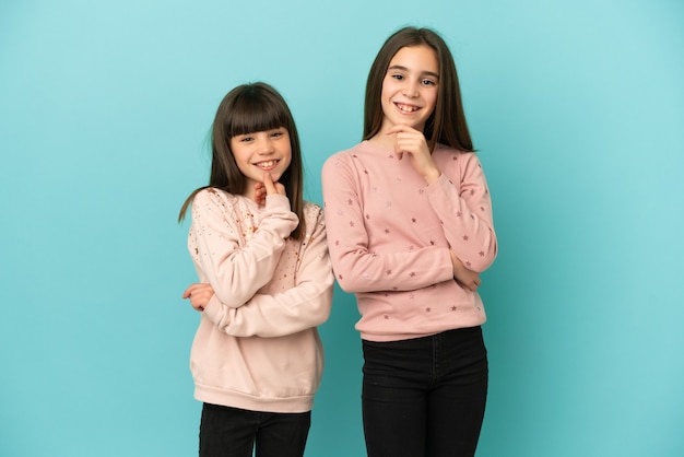 Hermanitas niñas aisladas sobre fondo azul sonriendo y mirando al frente con cara de confianza