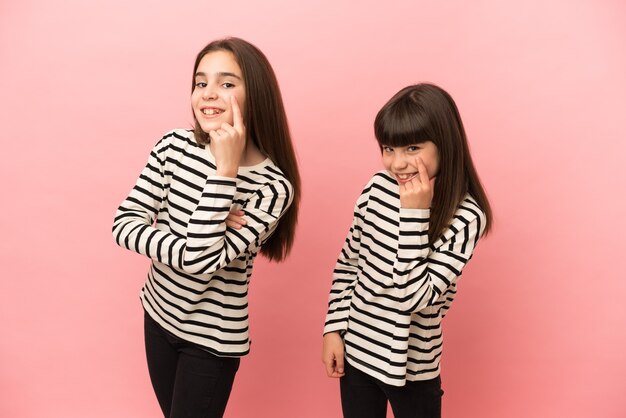 Hermanitas niñas aisladas sobre fondo rosa mirando hacia el frente