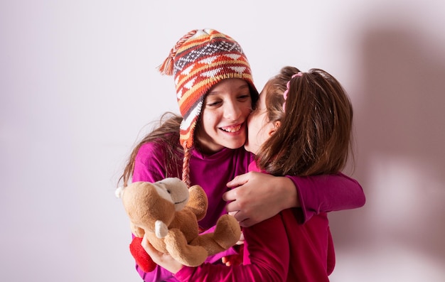 Las hermanitas que usan gorros de invierno y suéteres rojos pelean y pelean y compiten por un peluche