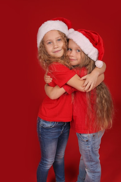 Hermanitas rubias con ojos azules, camisetas rojas con sombreros de santa claus abrazan