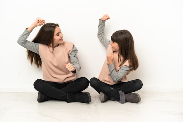 Hermanitas sentadas en el suelo aislado sobre fondo blanco celebrando una victoria en la posición ganadora