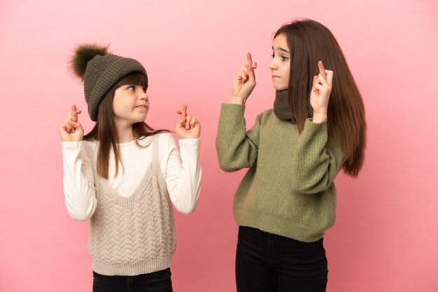 Hermanitas vistiendo una ropa de invierno aislada con los dedos cruzados y deseando lo mejor