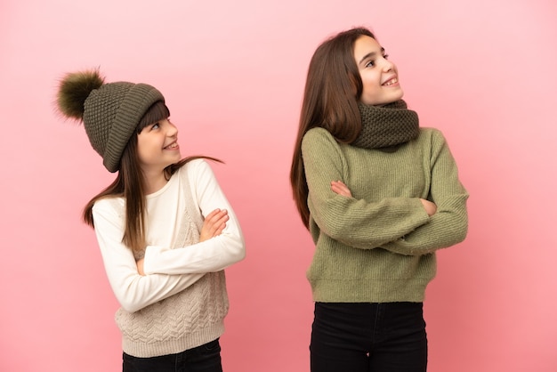 Hermanitas vistiendo ropa de invierno aislado sobre fondo rosa mirando hacia arriba mientras sonríe