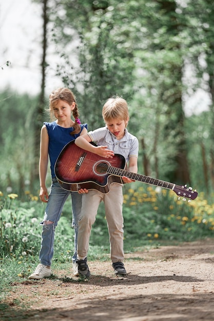 Hermanito y hermana con una guitarra para pasear por el parque de la ciudad. el concepto de una infancia feliz