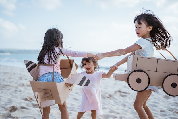 Hermano y amiga jugando con avión de cartón y coche en la playa