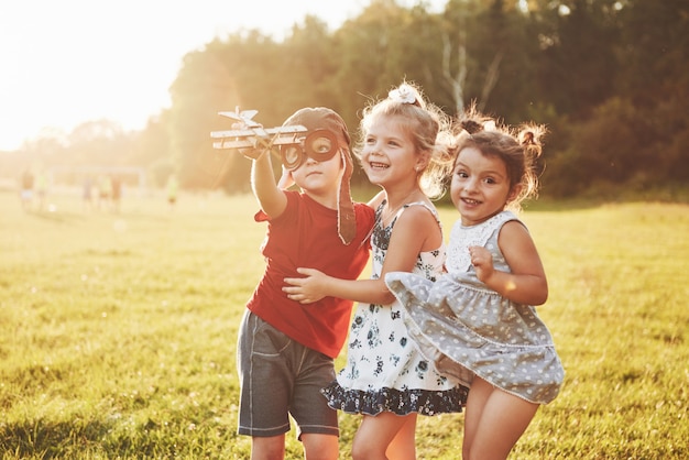 Foto hermano y dos hermanas están jugando juntos. tres niños jugando con un avión de madera al aire libre