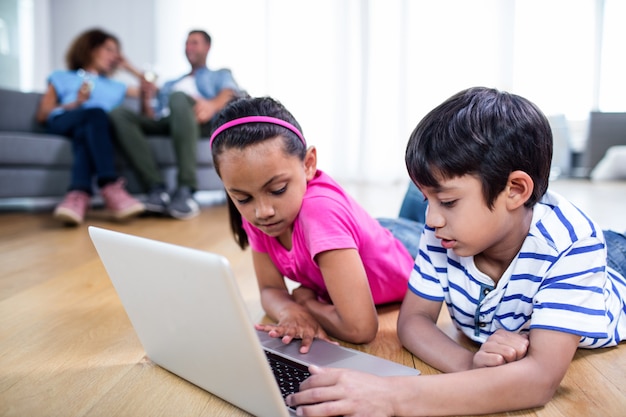 Hermano y hermana acostada en el piso y usando laptop