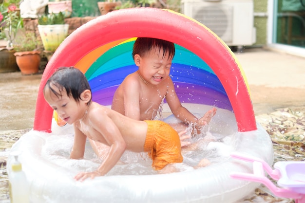 Hermano y hermana asiáticos divirtiéndose jugando con agua salpicando en la piscina inflable en casa