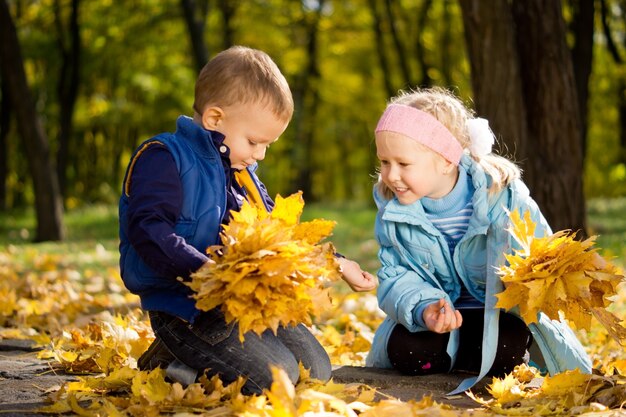 Hermano y hermana atractivo en otoño bosque arrodillado entre coloridas hojas amarillas caídas