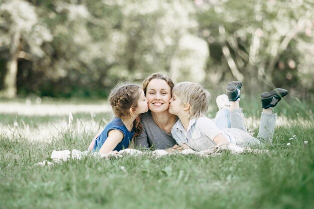 Hermano y hermana besando a mamá en el césped del parque