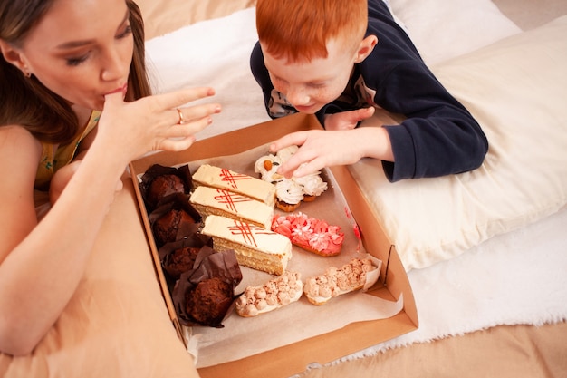 Hermano y hermana comen pasteles en la cama, se divierten