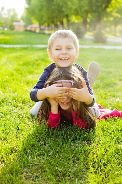 Hermano y hermana se divierten en el parque, los niños se establecen en la hierba verde, concepto de familia feliz