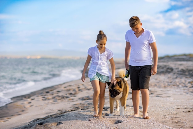 Hermano y hermana están caminando y con un perro de raza Akita Inu a lo largo de la costa del Mar Negro