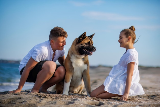 Hermano y hermana están caminando y con un perro de raza Akita Inu a lo largo de la costa del Mar Negro