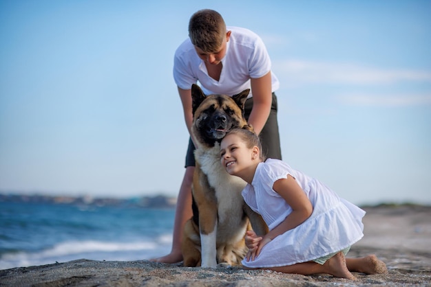 Hermano y hermana están caminando y con un perro de raza Akita Inu a lo largo de la costa del Mar Negro