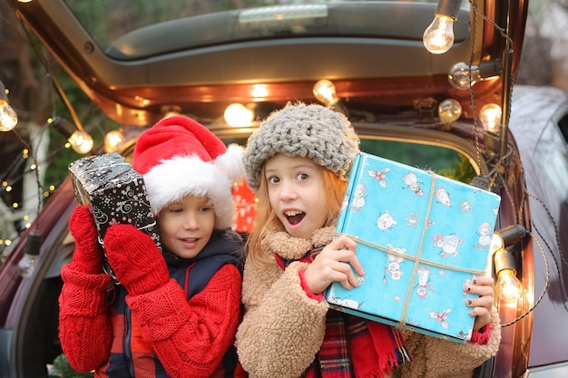 Foto hermano y hermana están sentados en el coche decorado con un montón de cajas de regalo de año nuevo