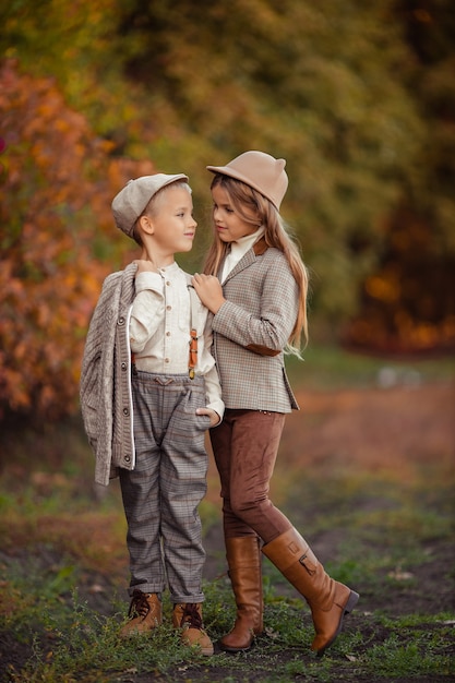 Hermano y hermana de hermosos niños con estilo en el otoño en un paseo por el parque