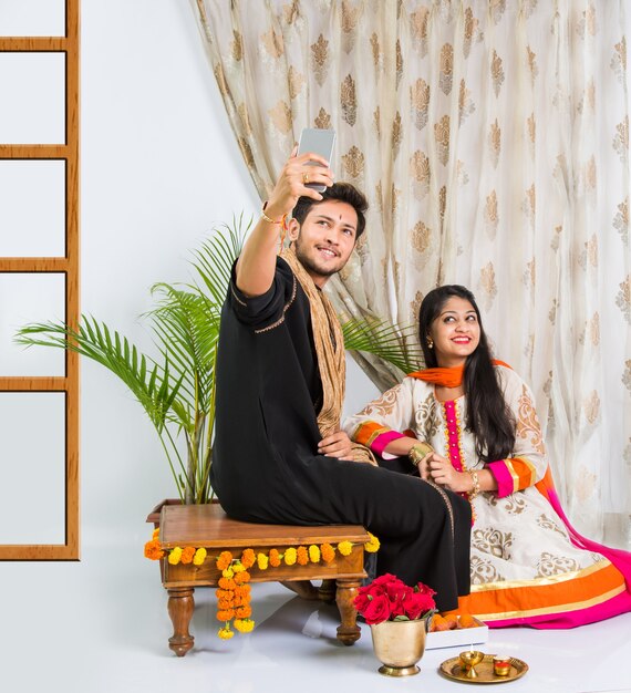 Hermano y hermana jóvenes indios celebrando el festival Raksha Bandhan o Rakhi o en Bhai dooj o Bhau-Beej con Poja Thali, dulces, regalos o tomando fotos selfie