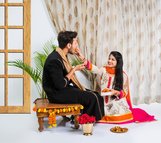 Hermano y hermana jóvenes indios celebrando el festival Raksha Bandhan o Rakhi o en Bhai dooj o Bhau-Beej con Poja Thali, dulces, regalos o tomando fotos selfie