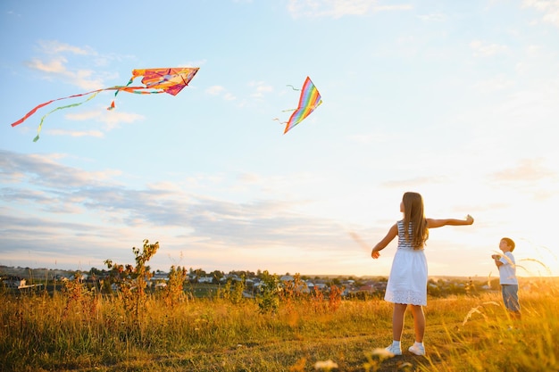 Hermano y hermana jugando con cometa y avión en el campo en la puesta de sol