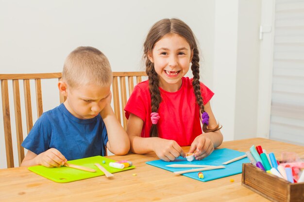 Hermano y hermana moldeando en la mesa en casa. El niño está triste porque no puede modelar tan bien como una niña mayor.