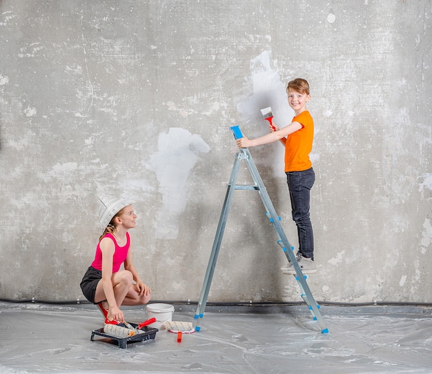 Hermano y hermana de niños felices hace reparaciones en casa Sonriente niño y niña pintando la pared