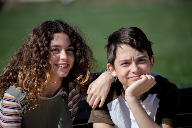 Hermano y hermana posan sentados en un banco del parque.
