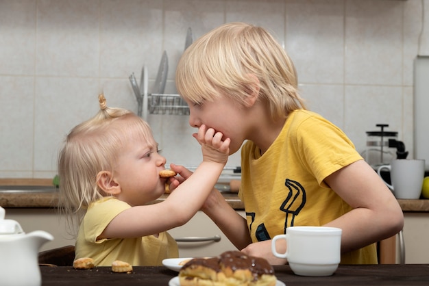 Hermano y hermana rubios se alimentan de galletas. Hermanos. Niños y dulces dañinos